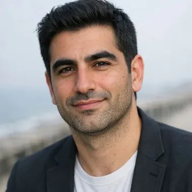 Man in late 30s, dark hair, olive skin, relaxed expression, coastal backdrop